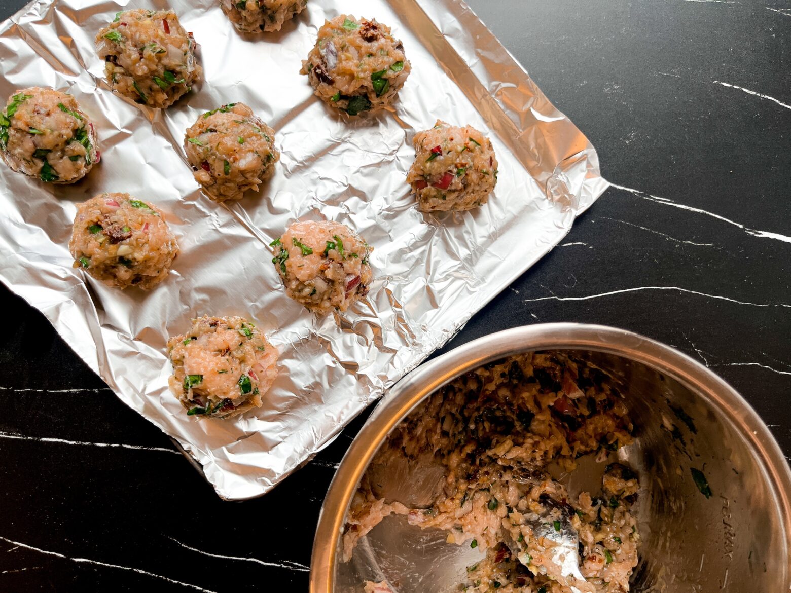 Mediterranean chicken meatball on a baking tray with a bowl of batter.