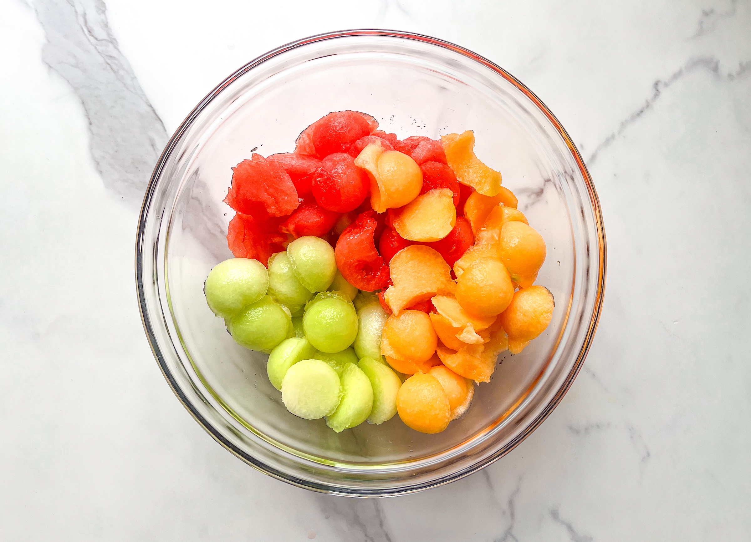 Watermelon, cantalope, and honeydew balls in a bowl being made into Melon Fruit Salad. 