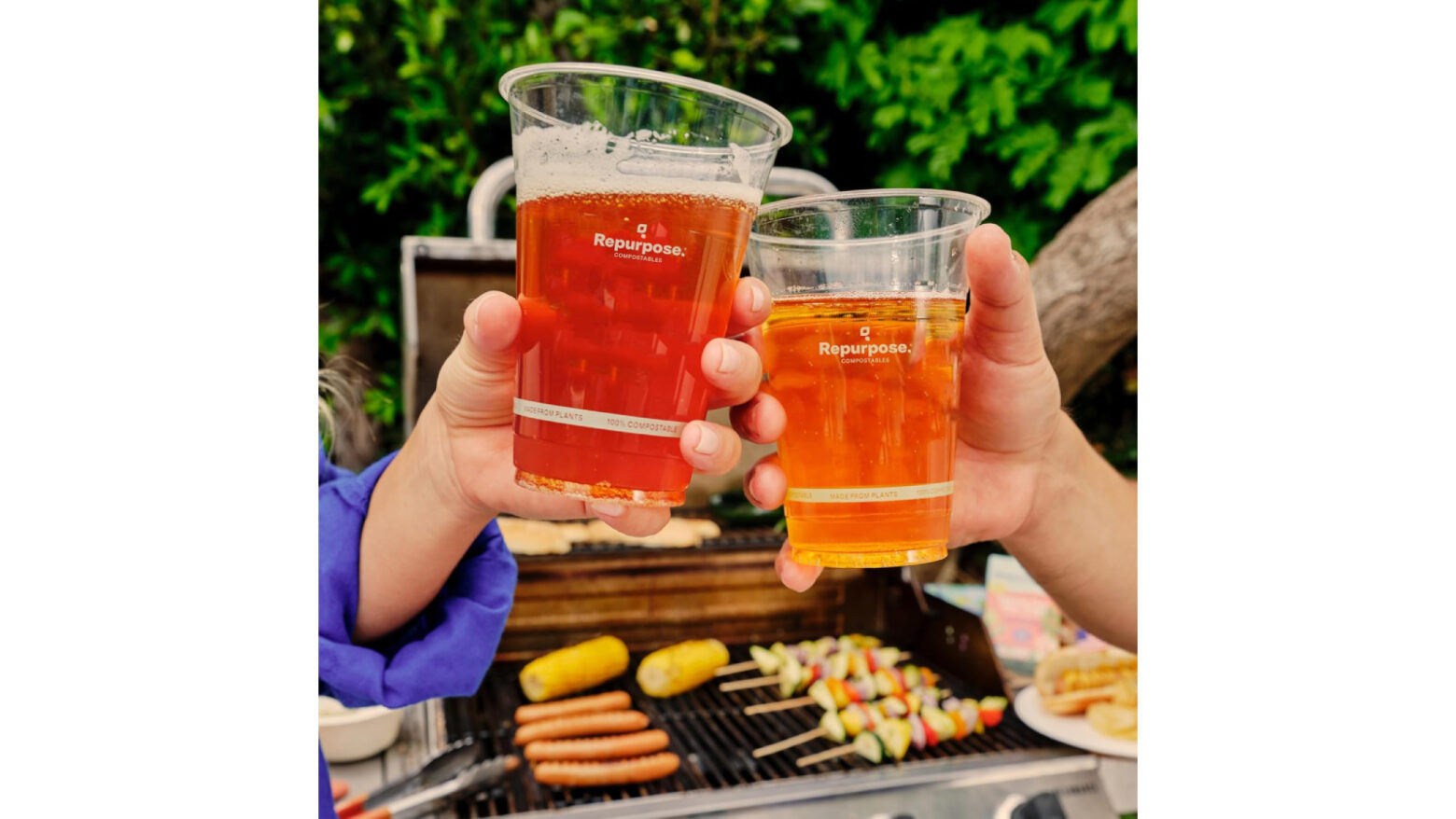 Closeup of two people giving a cheers with plant-based plastic cups over a grill with food.