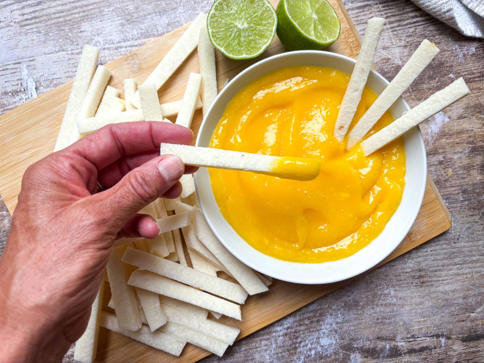 Hand holding a jicama stick dipped in mango sauce.