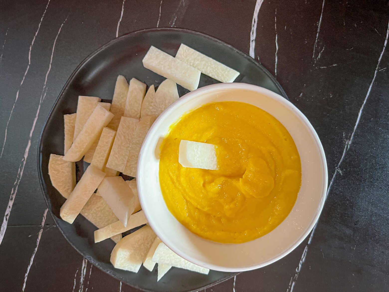 Jicama sticks with mango dip, with one stick in the dip.