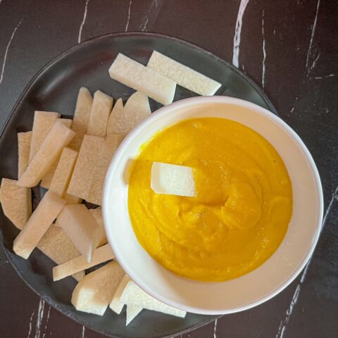 Jicama sticks with mango dip, with one stick in the dip.