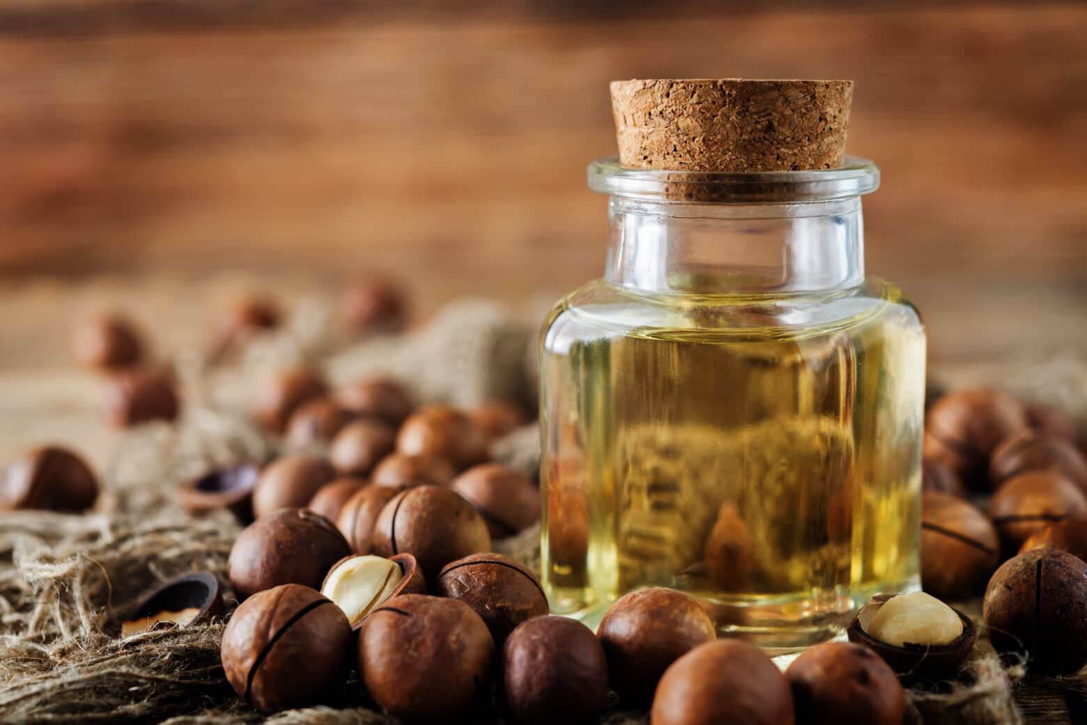 Macadamia oil in a jar, surrounded by whole macadamia nuts.