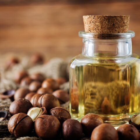 Macadamia oil in a jar, surrounded by whole macadamia nuts.