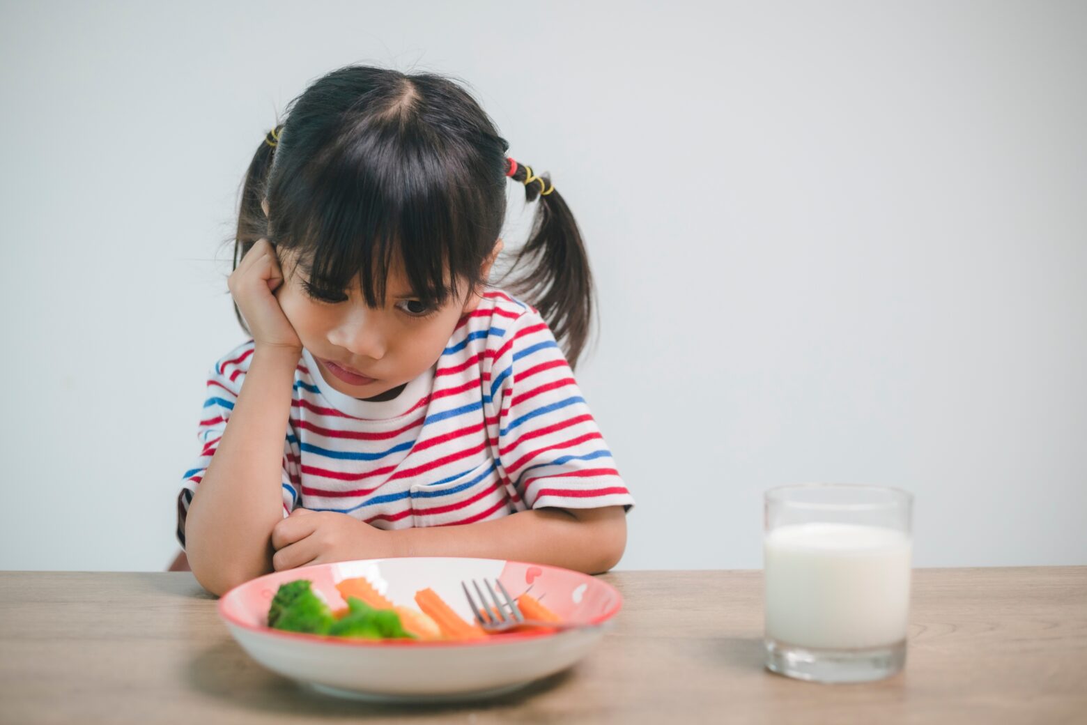 A young girl pouts over a bowl of vegetables.
