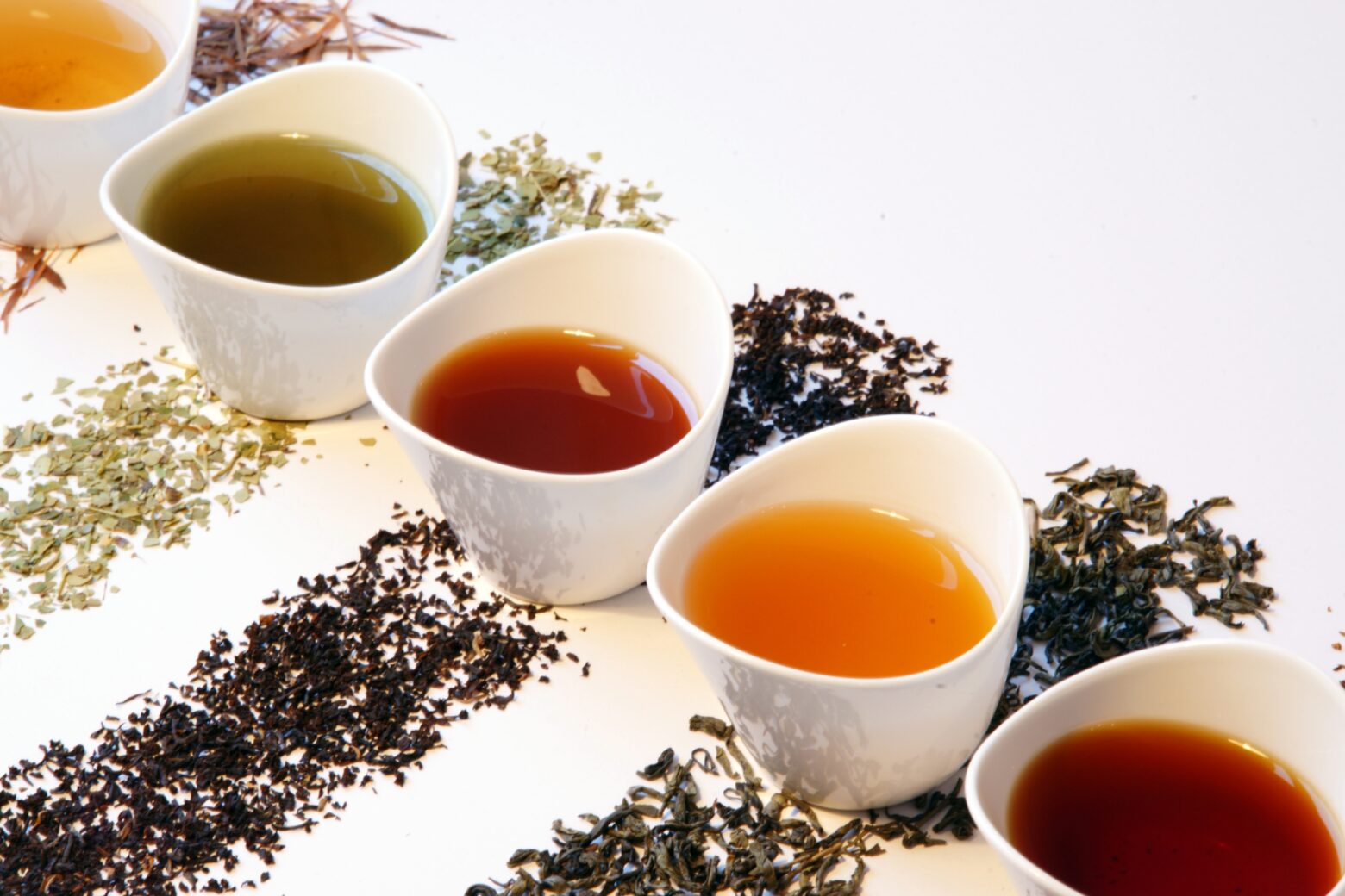 A line of various types of tea in white teacups.
