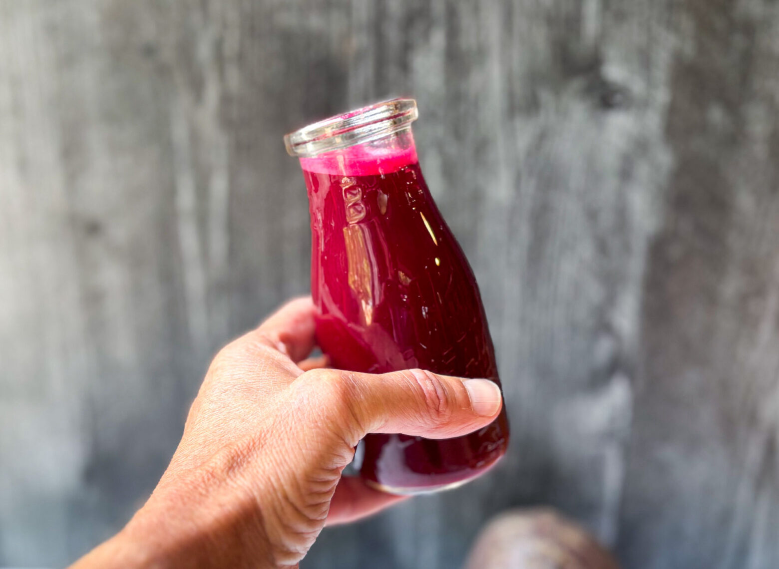 Glass of beet juice held against a grey background.