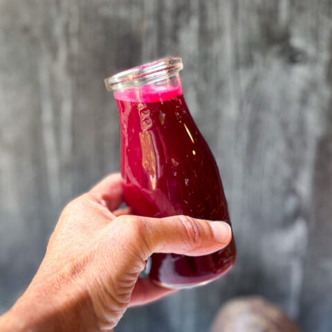 Glass of beet juice held against a grey background.
