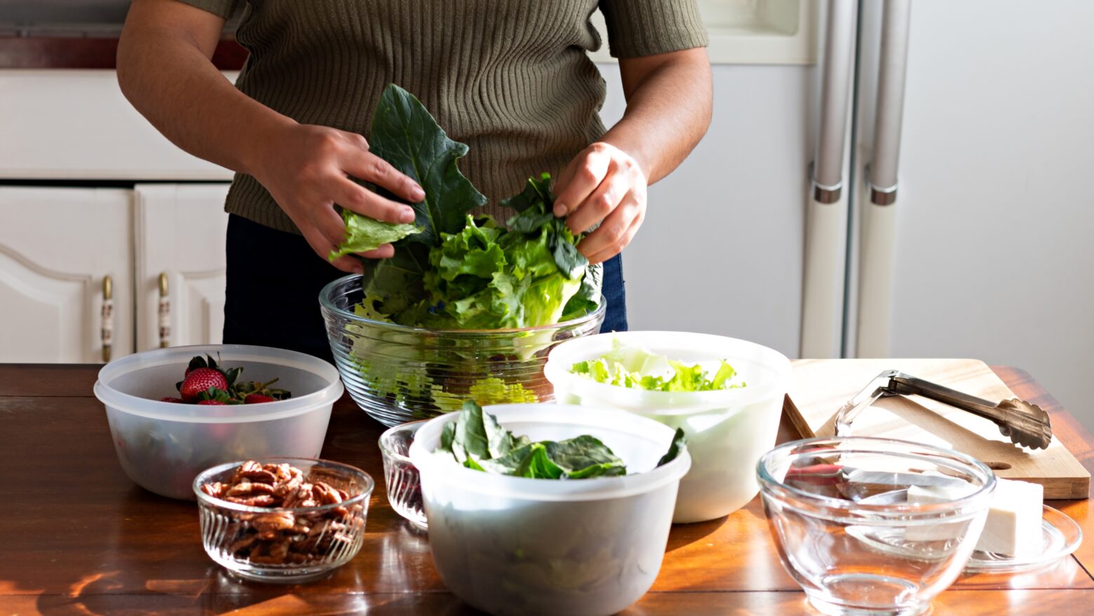 Cropped image of a woman mixing different salad ingredients into a bowl with her hands.