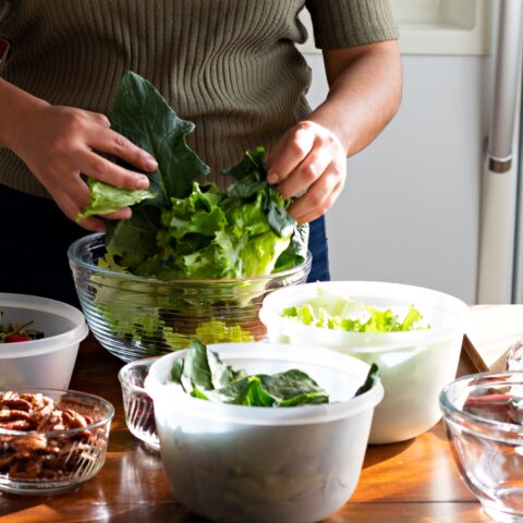Cropped image of a woman mixing different salad ingredients into a bowl with her hands.
