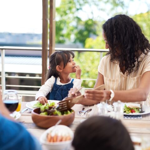 A mother and young daughter share a moment while having a healthy lunch outside.