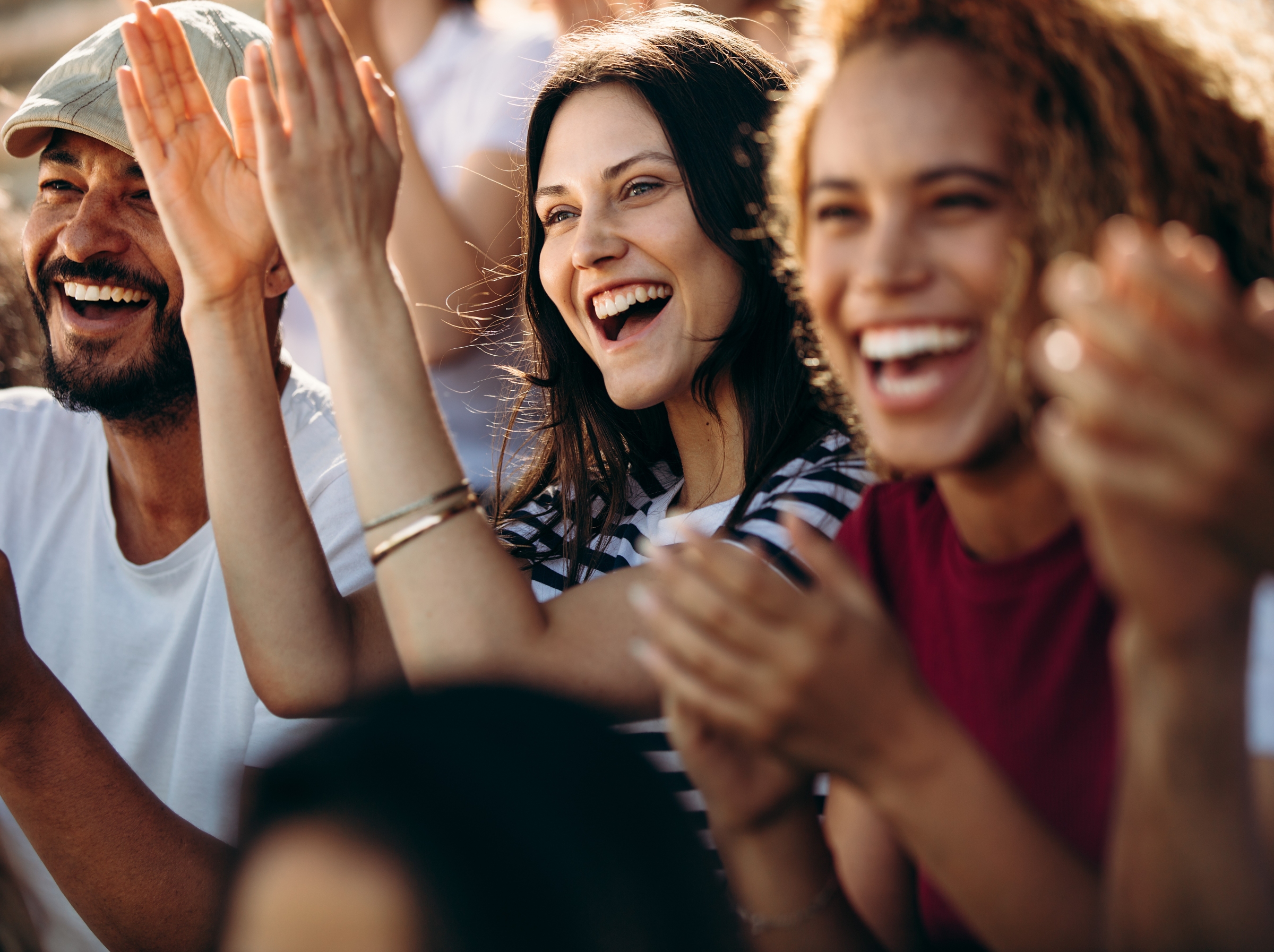 A crowd of people clapping and smiling in the sunshine.