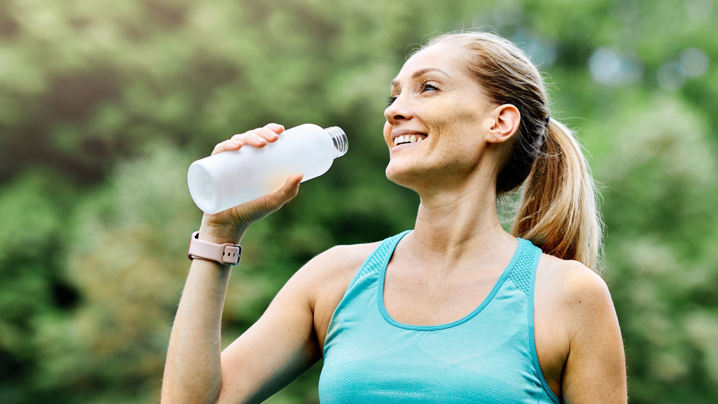 A woman smiling and drinking water during a workout.