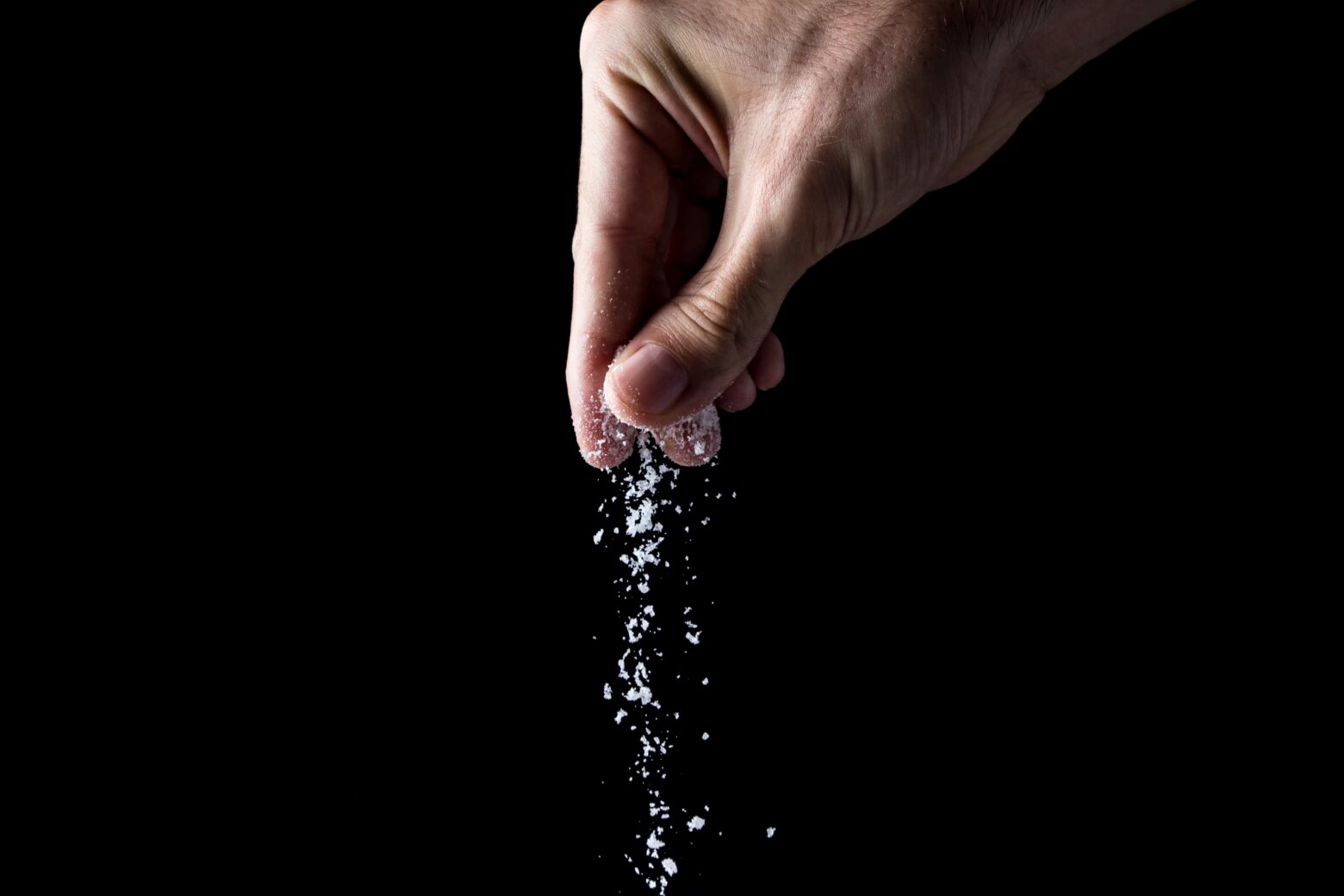 Hand sprinkling salt against a black background.