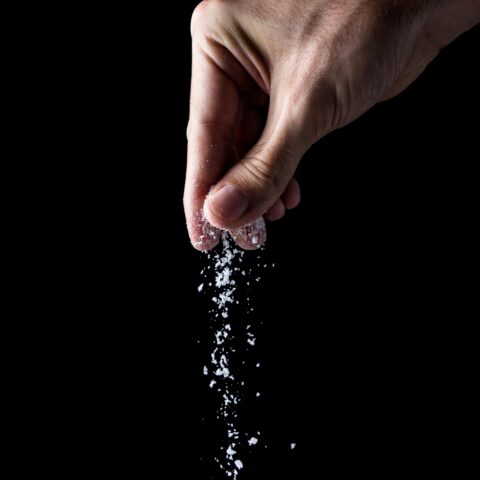 Hand sprinkling salt against a black background.