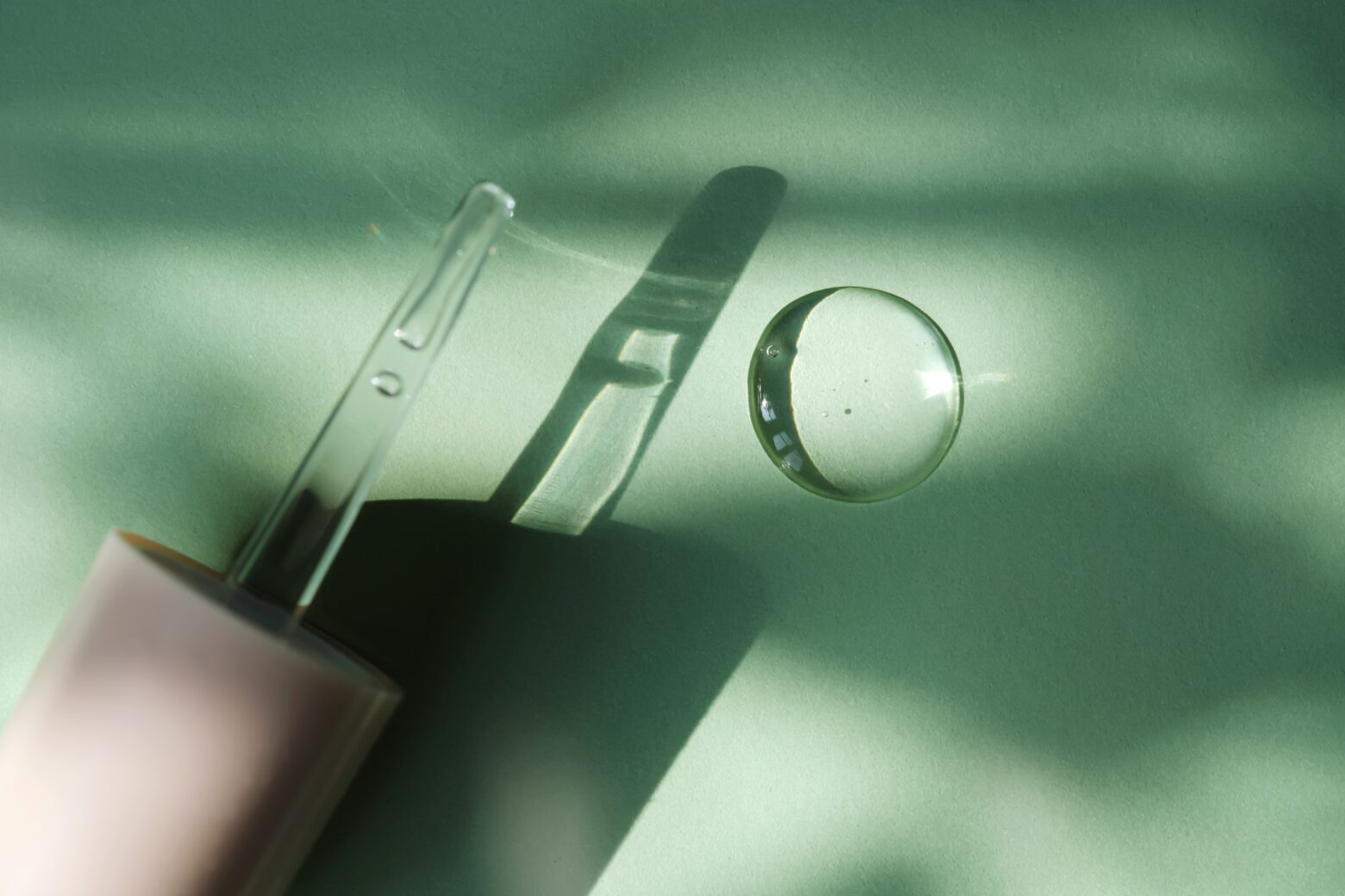 Glass dropper and a spot of clear snail mucin serum on a sage background