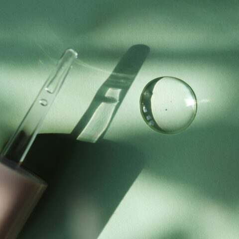 Glass dropper and a spot of clear snail mucin serum on a sage background