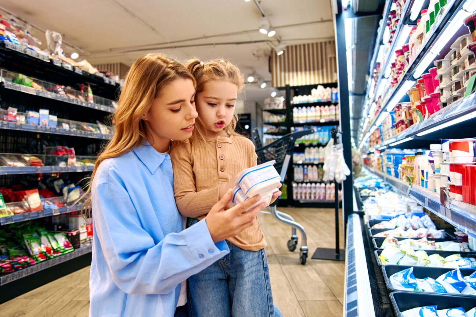 A mother and her daughter examine a package together while shopping at a grocery store.