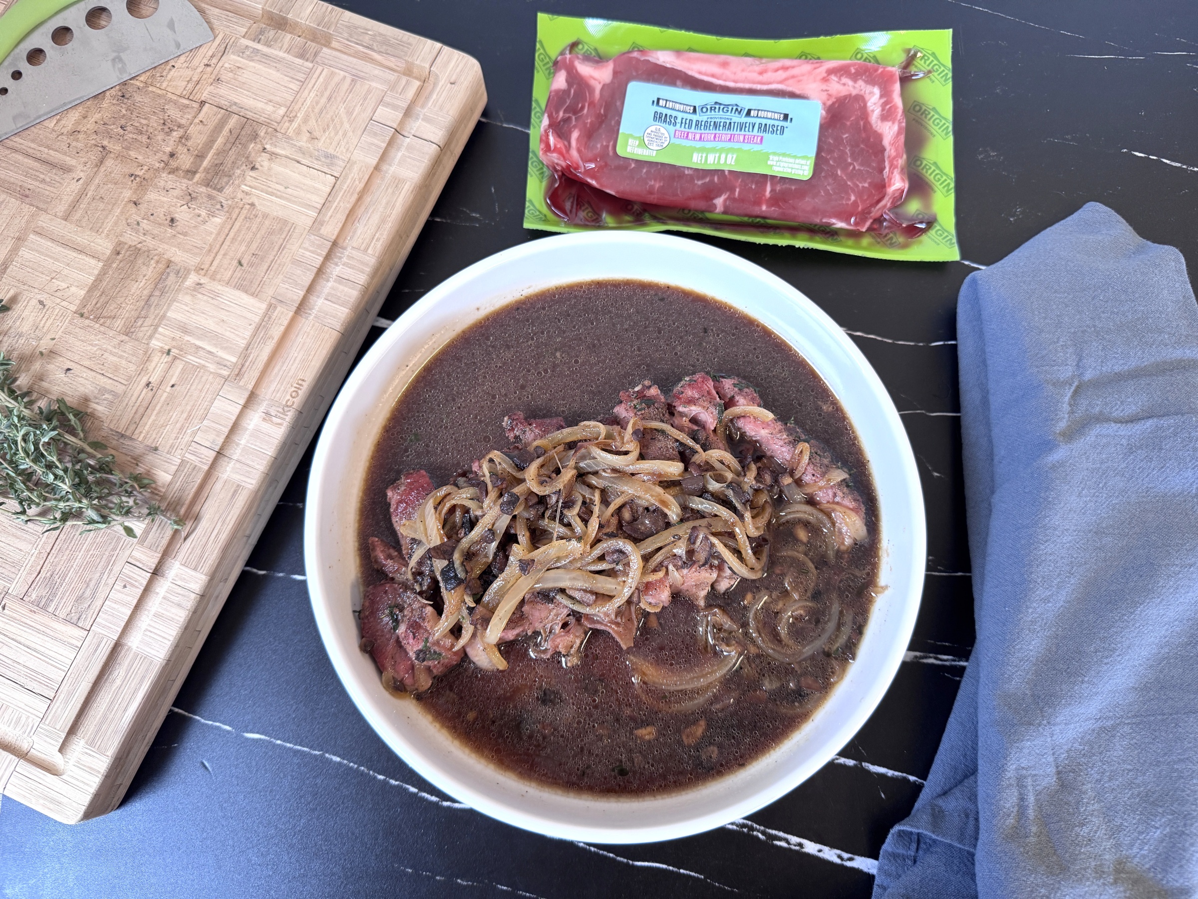 Above shot of plated French Onion Steak with raw Origin Provisions packaging nearby.