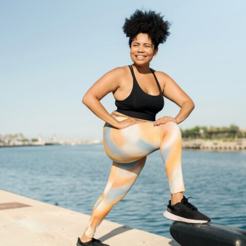 A woman stretching by a body of water before starting her workout.