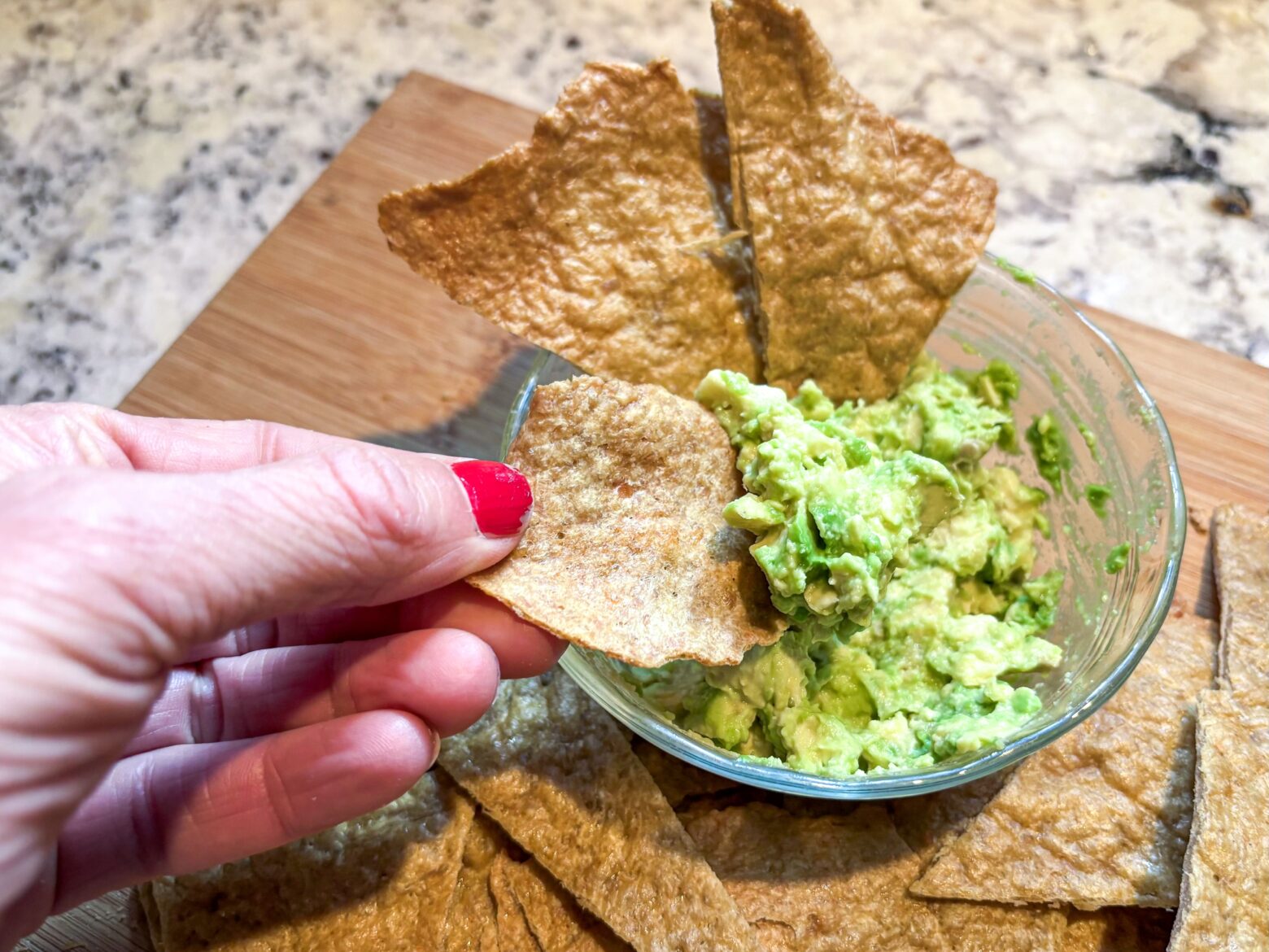 Hand holding a chicken chip with a scoop of guacamole.