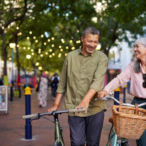 Older couple walking bikes down a sidewalk.