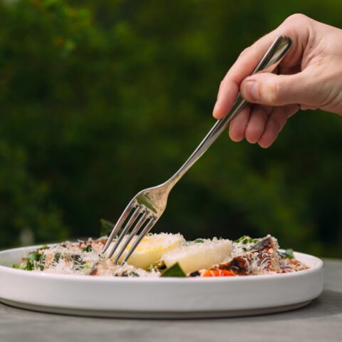 A hand reaching from out of frame to stab a piece of food with a fork.