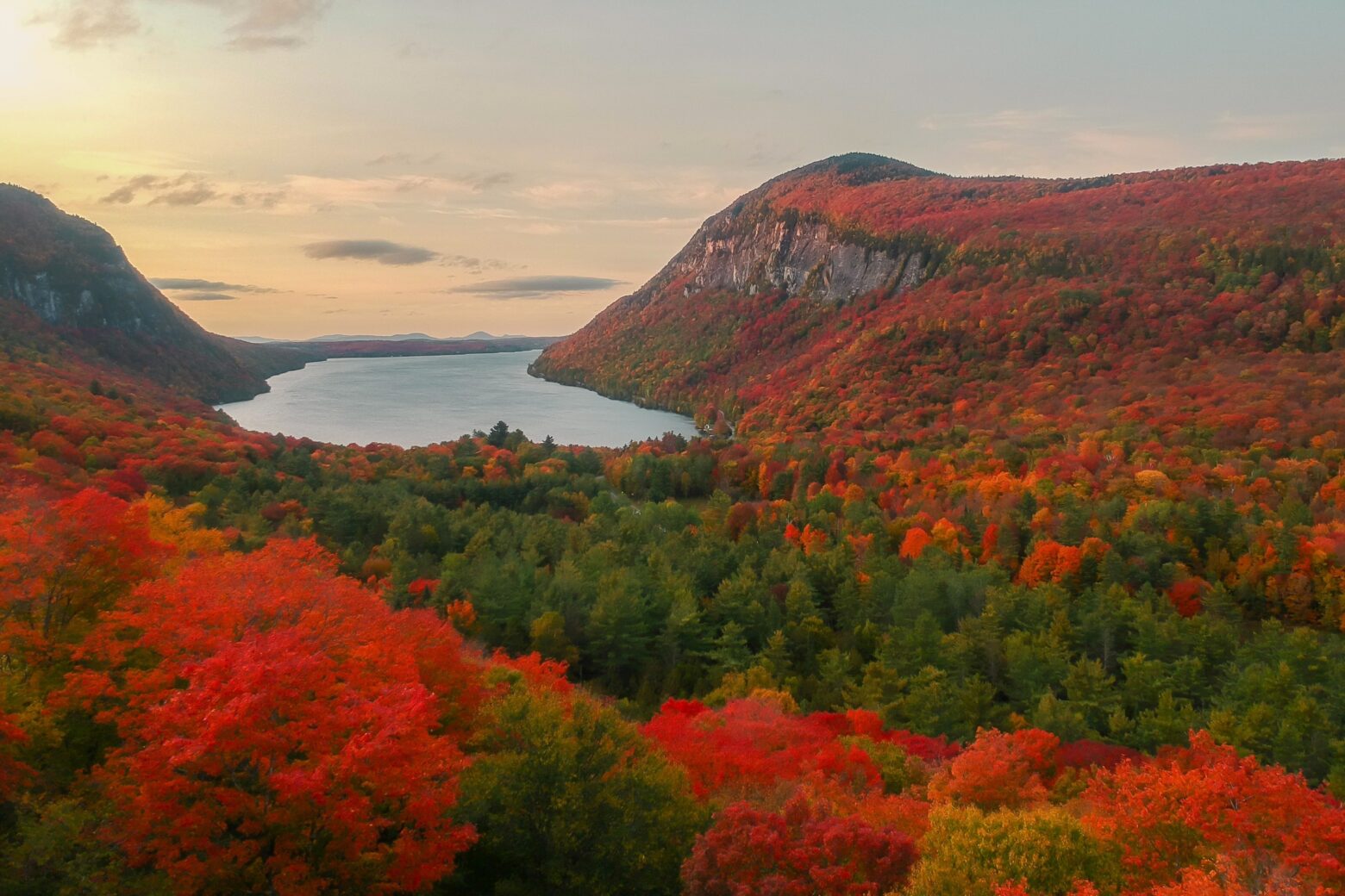 A lake nestled in a hilly landscape covered in brilliant red fall foliage.