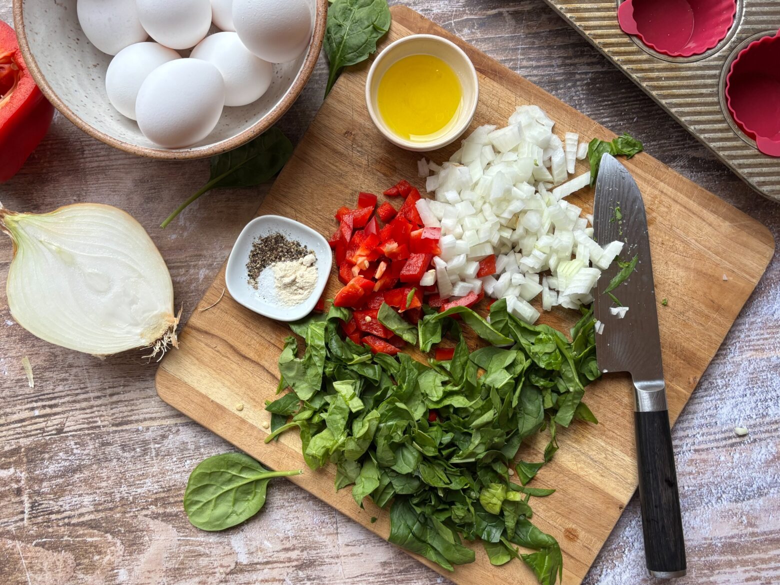 Spinach, onion, and bell pepper chopped on a cutting board surrounded by other ingredients.