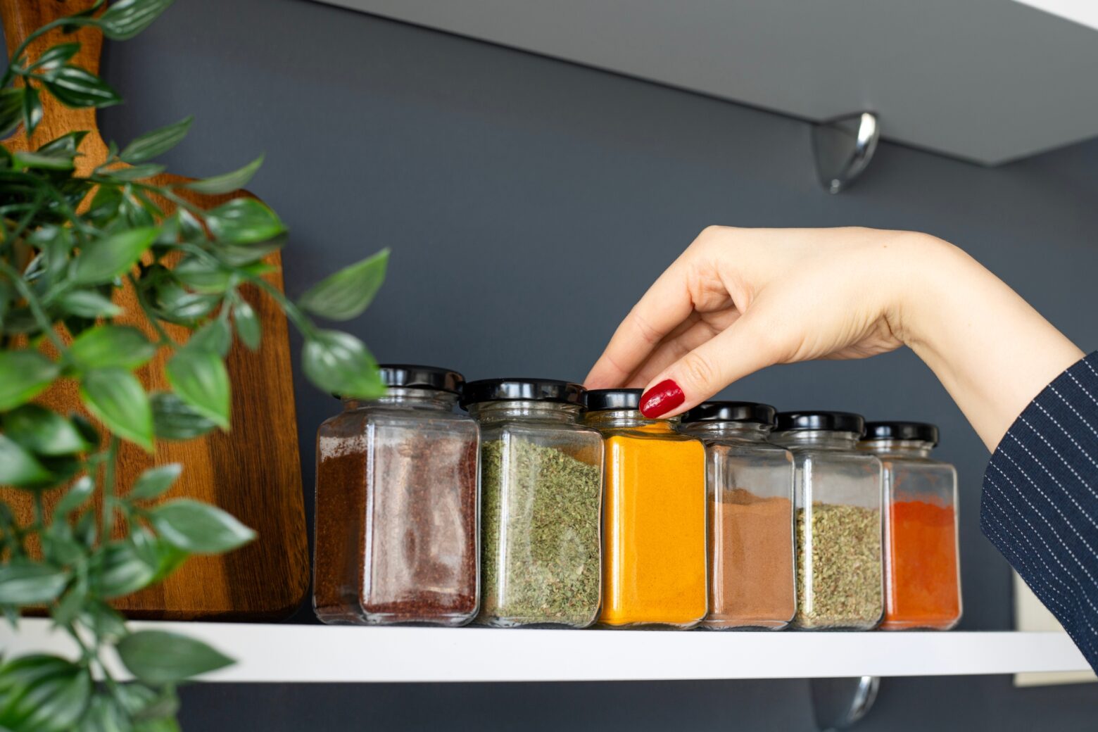 Hand reaching onto spice rack to grab a jar of turmeric.