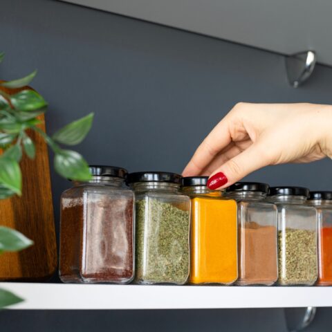 Hand reaching onto spice rack to grab a jar of turmeric.