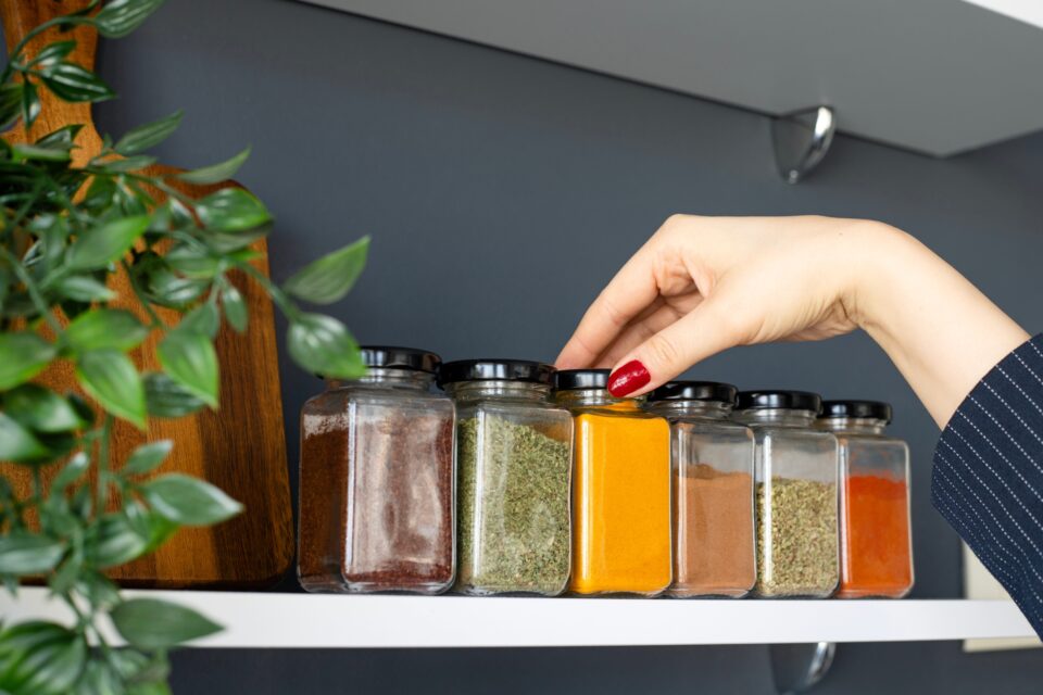 Hand reaching onto spice rack to grab a jar of turmeric.