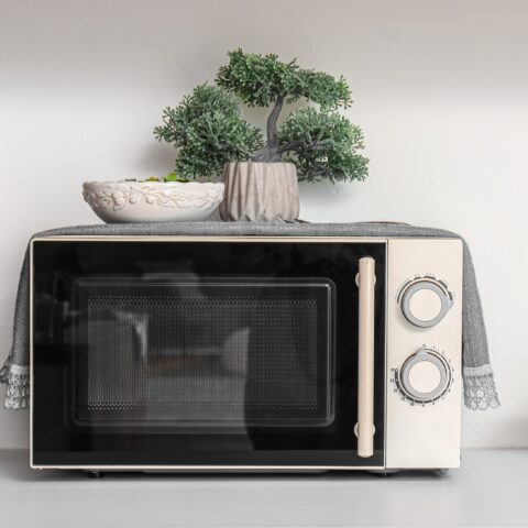 Microwave on a countertop with a fake bonsai on top.