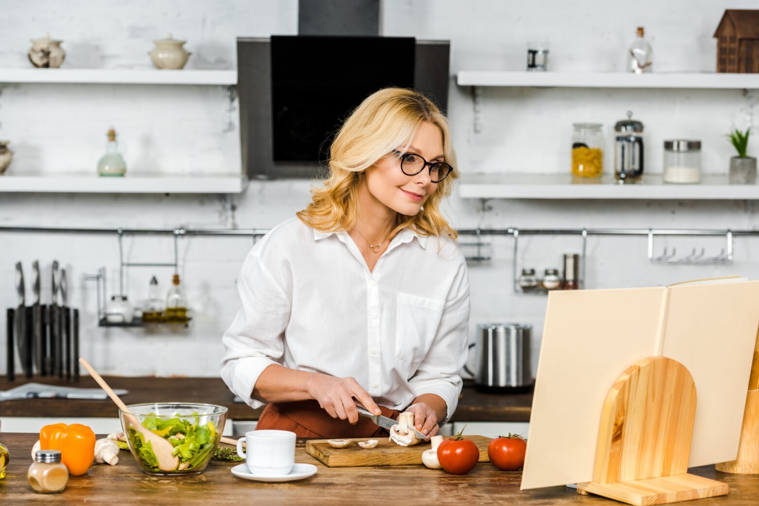 Mature woman smiling in her kitchen as she cuts mushrooms for a recipe.