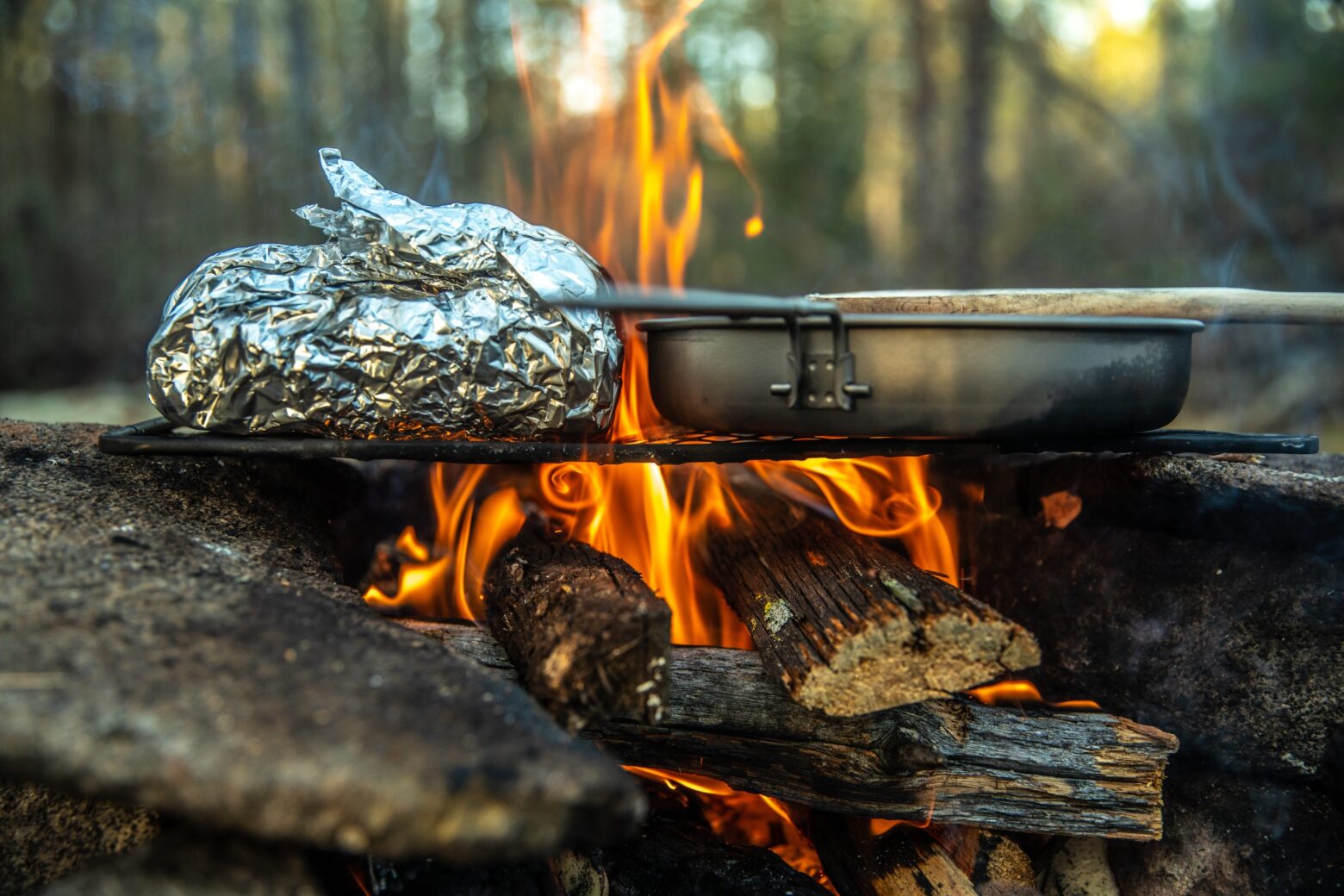 A pan and a wrapped meal over a campfire.