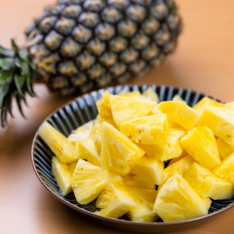 Whole pineapple next to a bowl of pineapple slices.