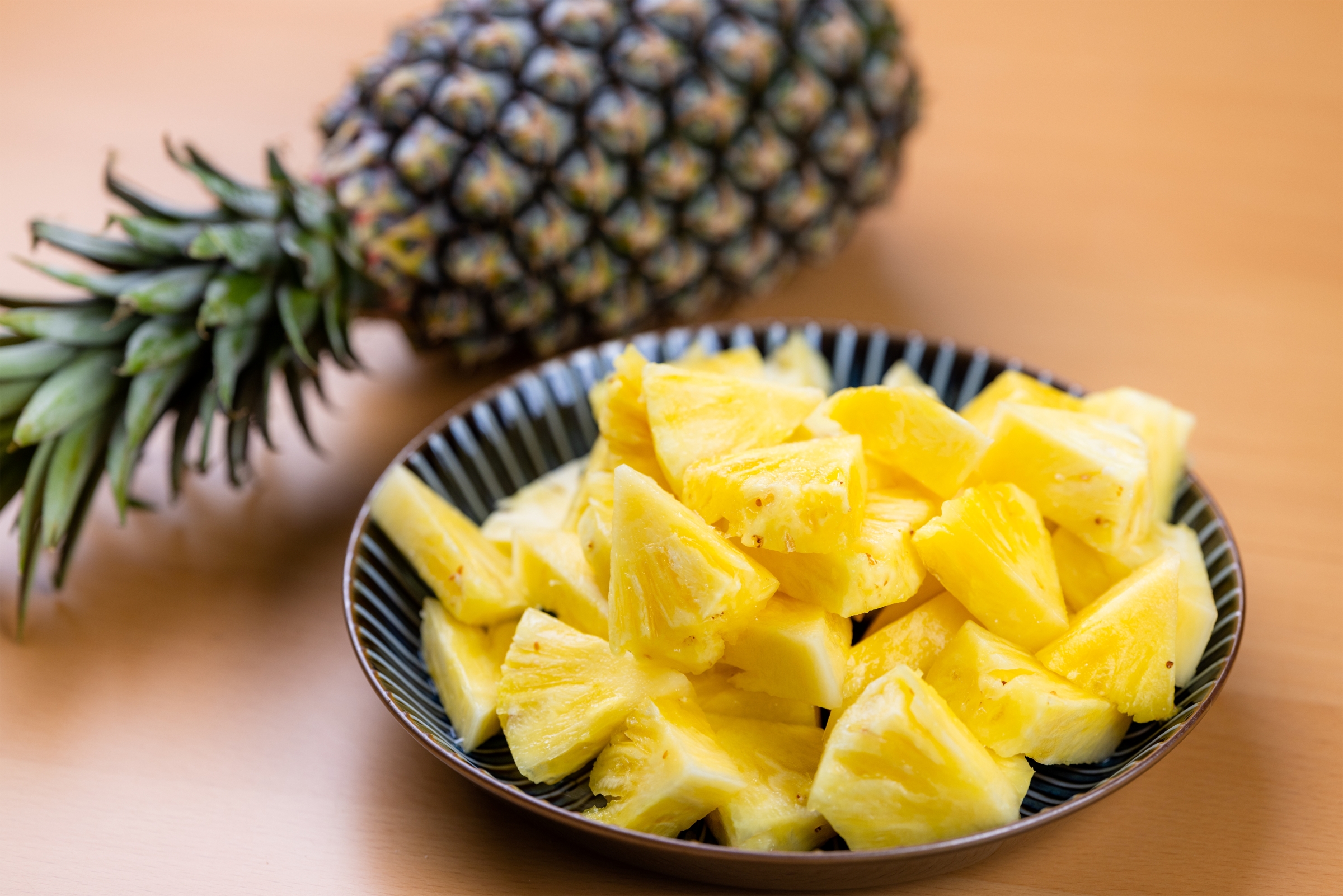 Whole pineapple next to a bowl of pineapple slices.