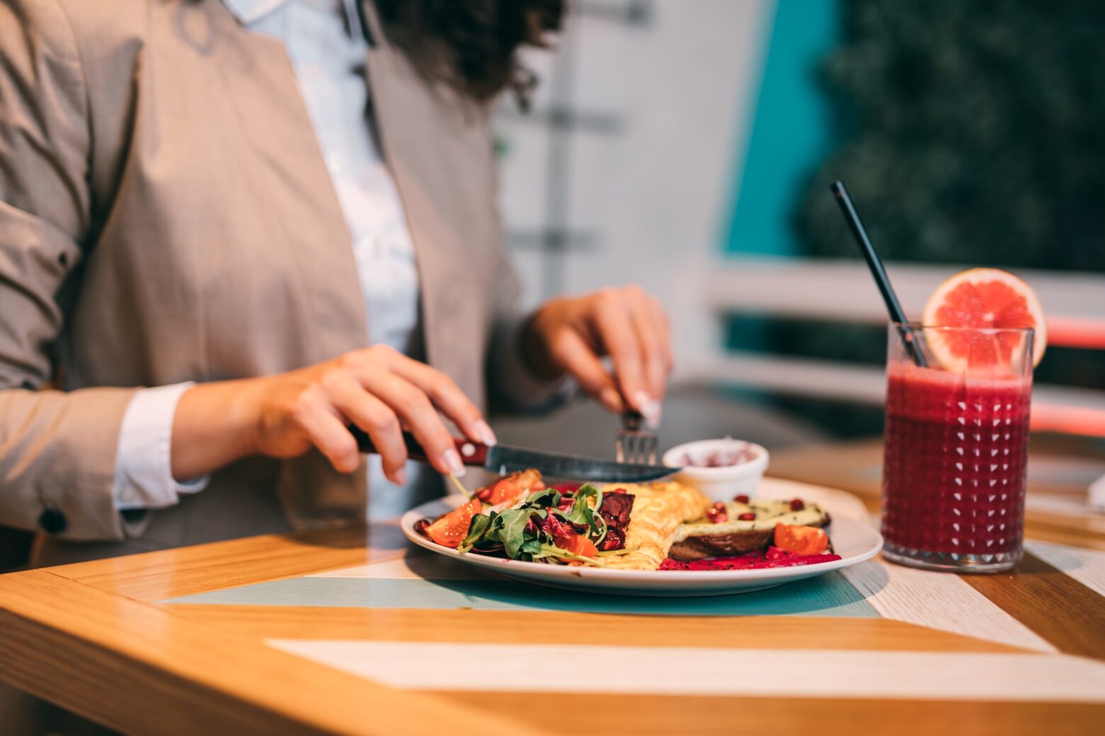 Close-up of a woman eating a vibrant dinner with a tropical drink.