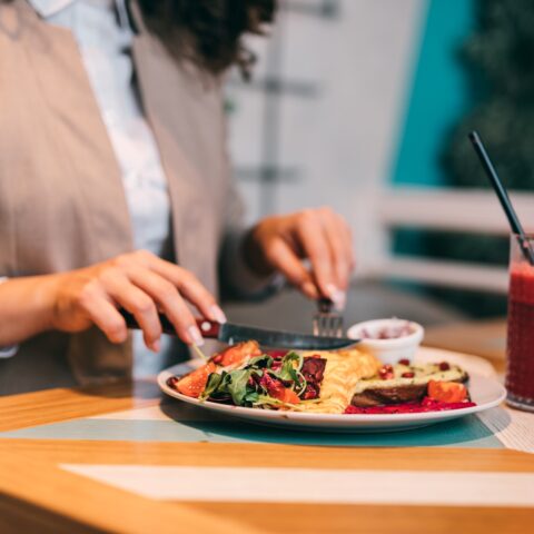 Close-up of a woman eating a vibrant dinner with a tropical drink.