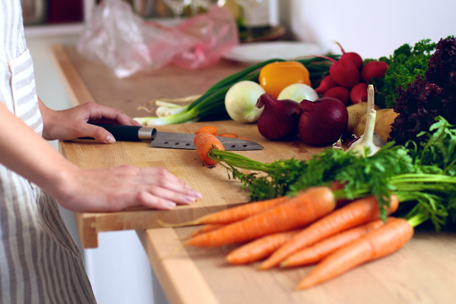 A woman stands at a cutting board, ready to prep a variety of fresh vegetables.