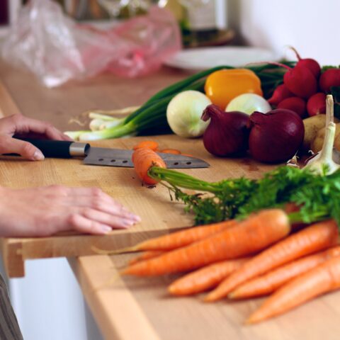 A woman stands at a cutting board, ready to prep a variety of fresh vegetables.