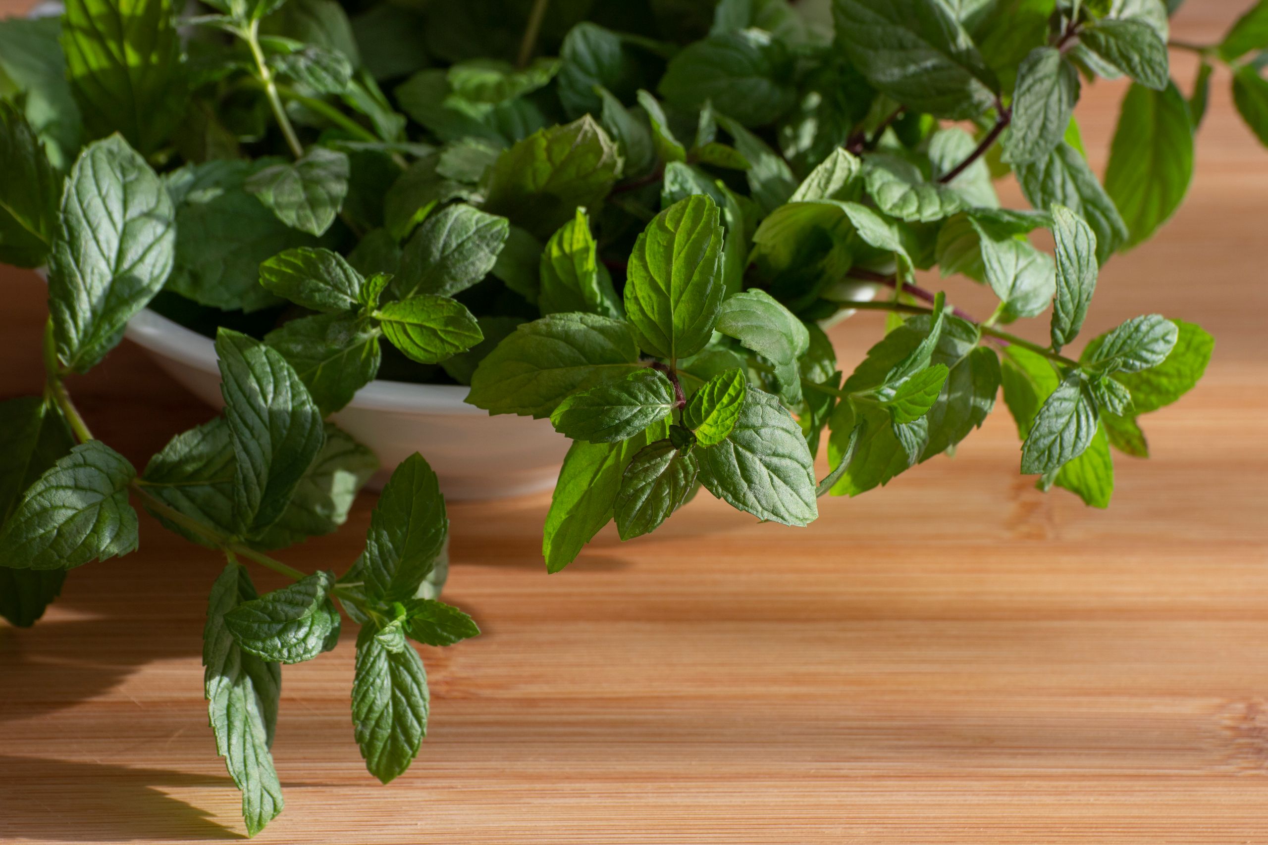 Close-up of fresh mint leaves in a bowl on a wooden surface, top view.