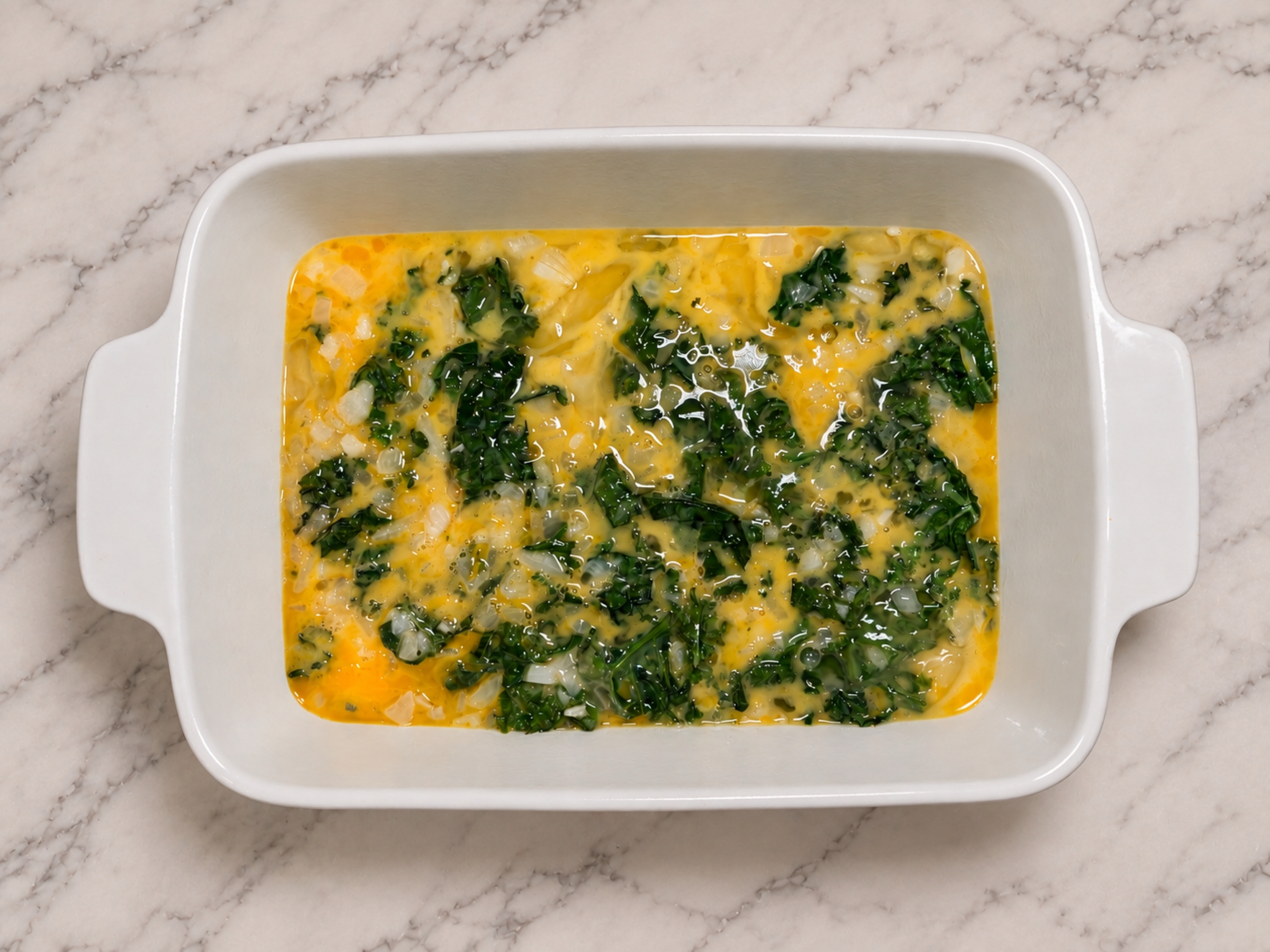 Egg batter and kale in a baking dish.