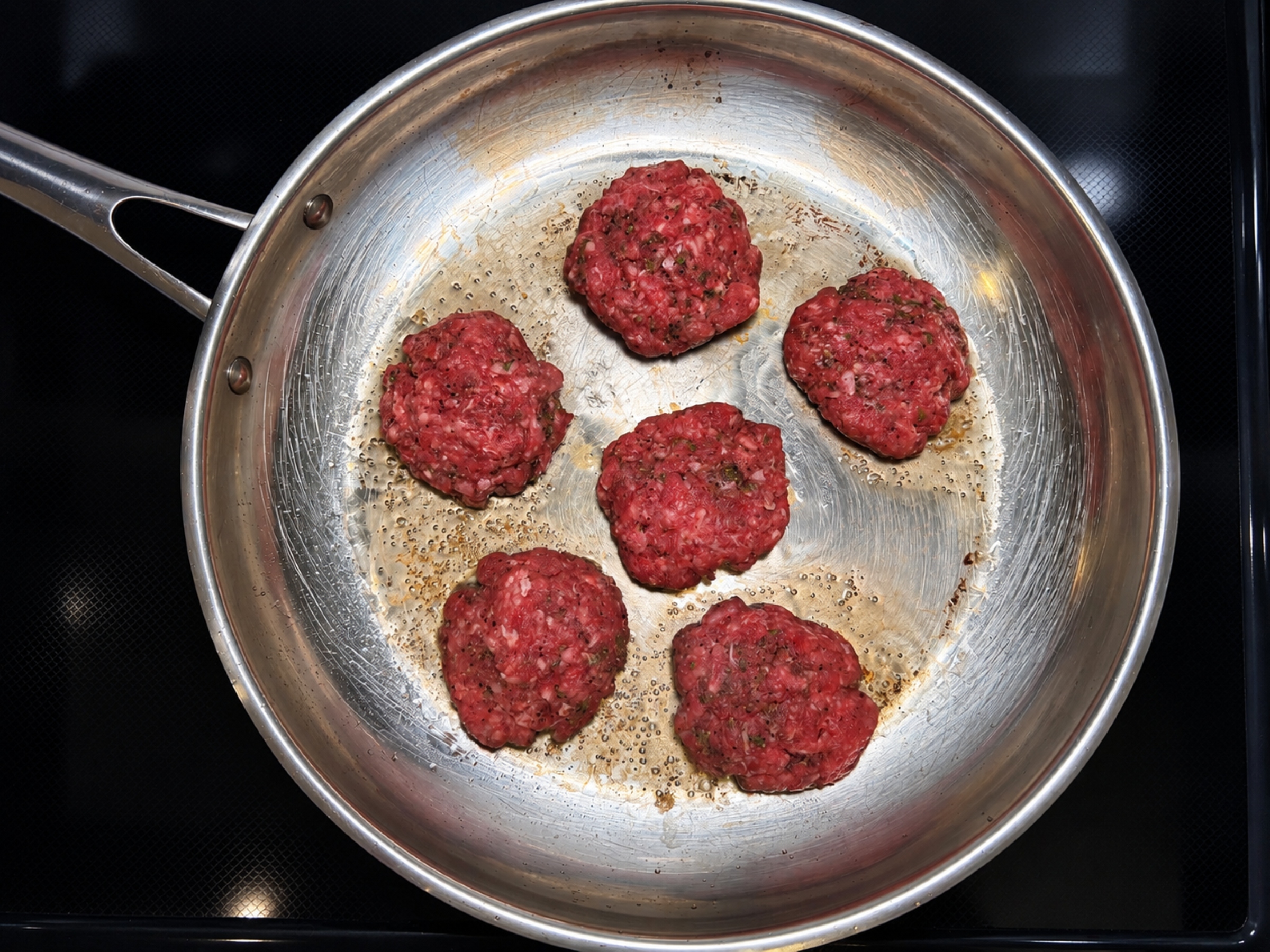Bison patties cooking in a pan.