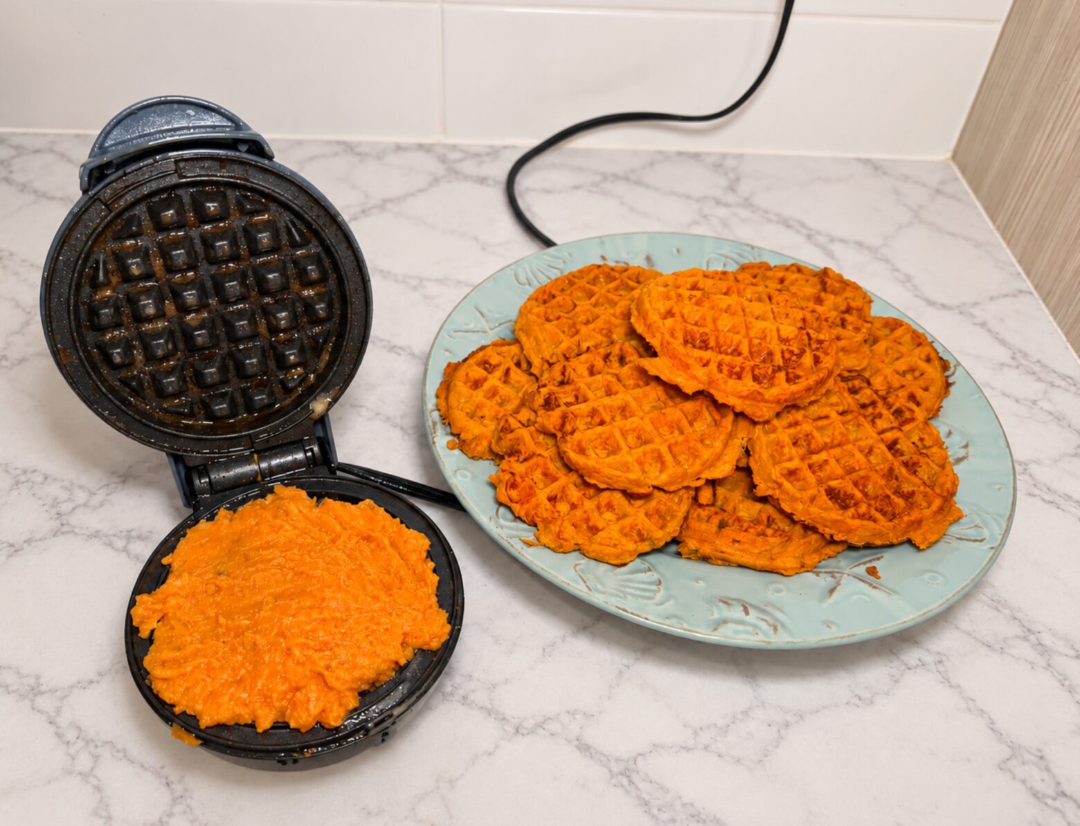 Finished sweet potato waffles next to a waffle iron.